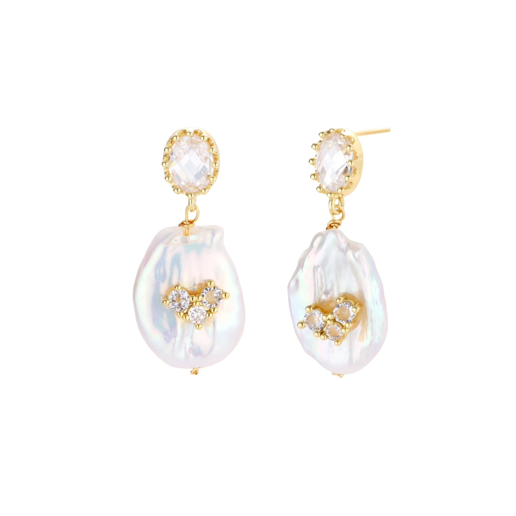 Gold-plated drop earrings with iridescent baroque pearls and crystal flower accents on cream background