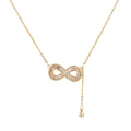 Gold infinity pendant with baguette crystals on adjustable chain against cream background.
