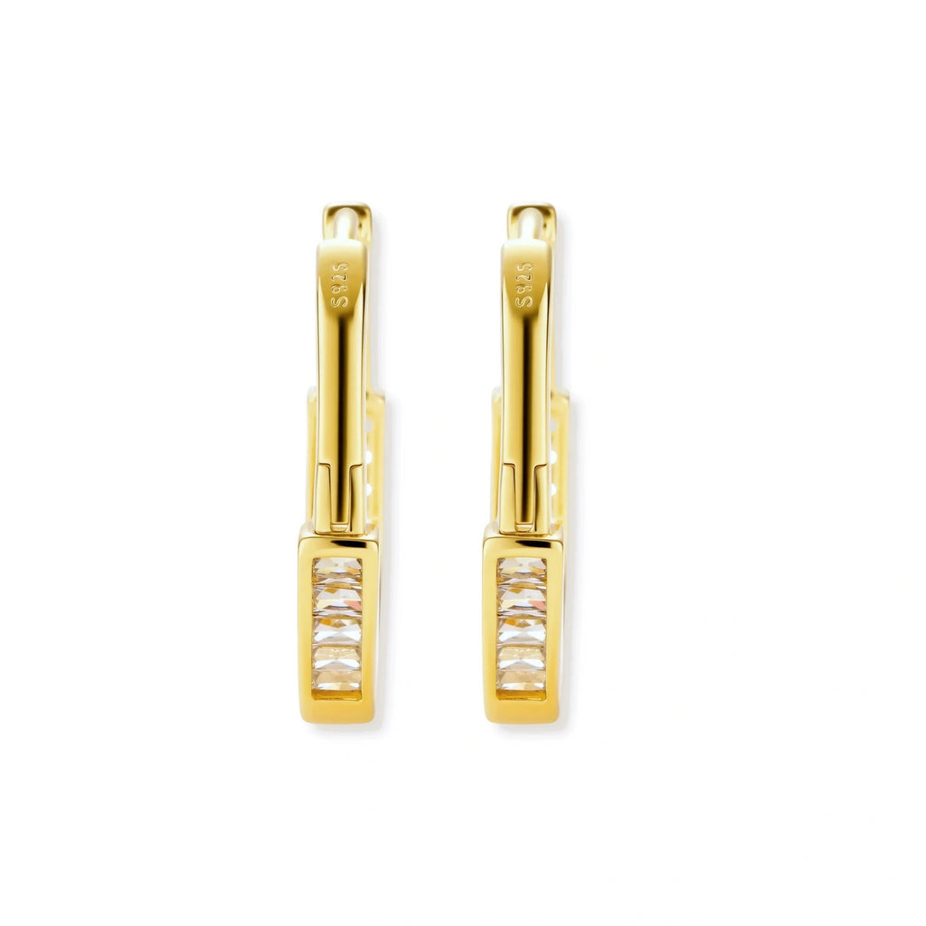 Close-up of gold-plated sterling silver huggie hoop earrings featuring rectangular cubic zirconia stones on neutral background.